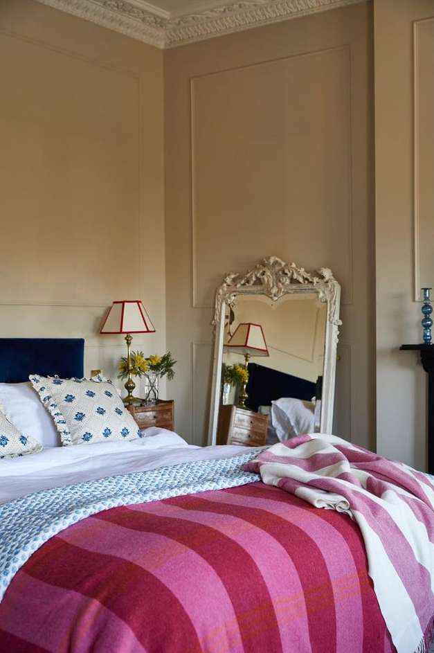 Bedroom interior showcasing a neatly made bed with a striped blanket, a decorative mirror, and bedside lamps, creating a cozy atmosphere.