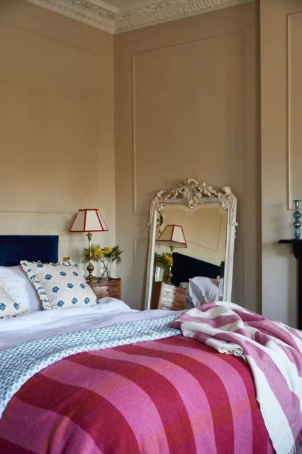 Bedroom interior showcasing a neatly made bed with a striped blanket, a decorative mirror, and bedside lamps, creating a cozy atmosphere.