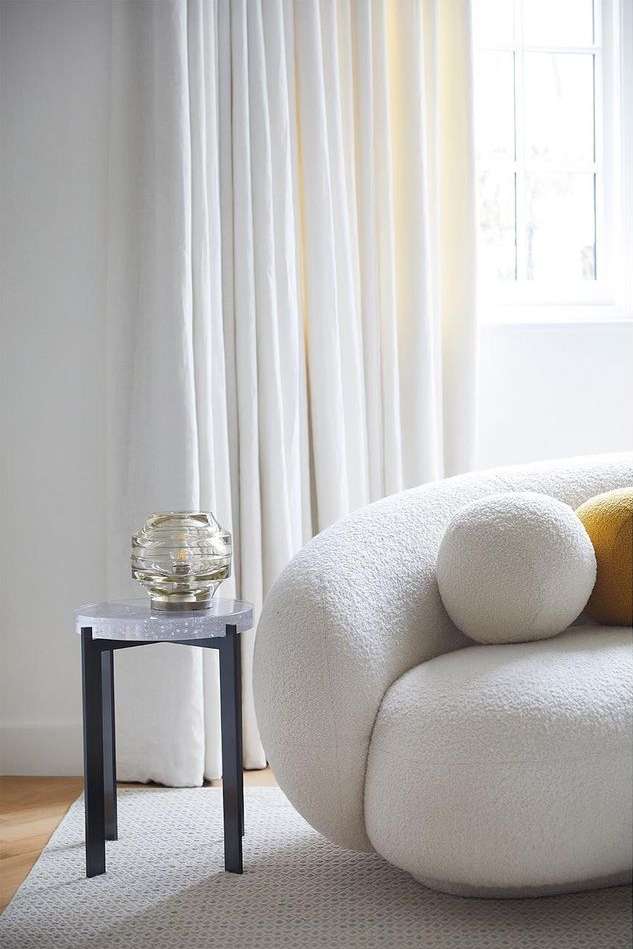 Interior shot of a living room featuring a white bouclé sofa, round accent pillows, and a modern end table with a transparent lamp.