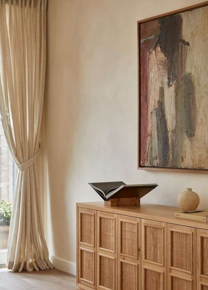 Contemporary interior featuring a wooden cabinet with an open book, abstract art, and natural light from a nearby window.