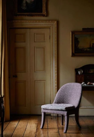 Upholstered purple patterned armchair resting on a wooden floor in a dimly lit traditional interior by Helen Cathcart