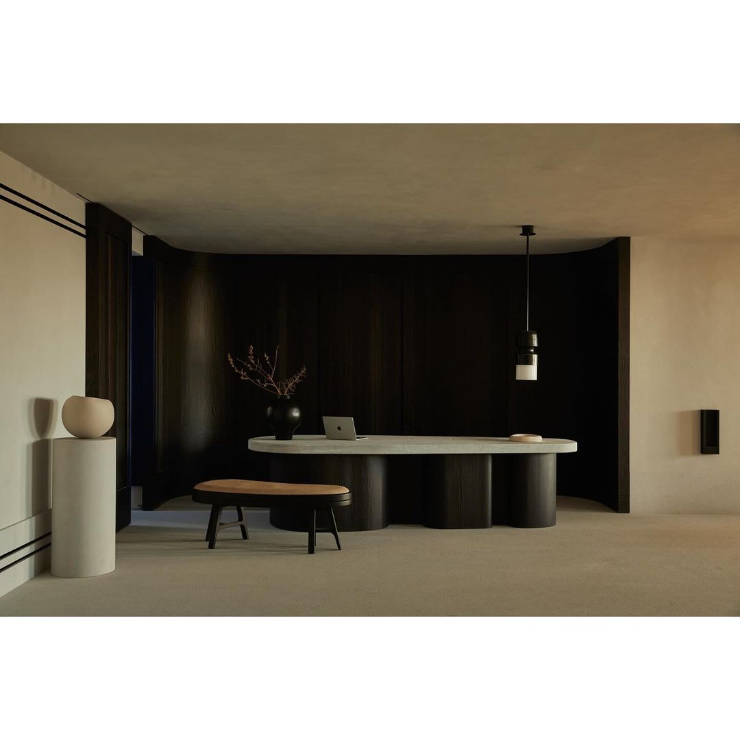Modern interior space featuring a table as a desk, decorative objects, a wooden bench, and dark wood wall paneling with warm lighting.
