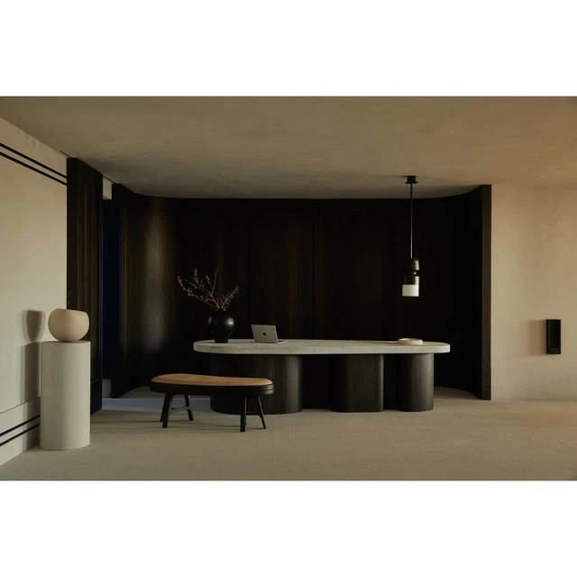 Modern interior space featuring a table as a desk, decorative objects, a wooden bench, and dark wood wall paneling with warm lighting.