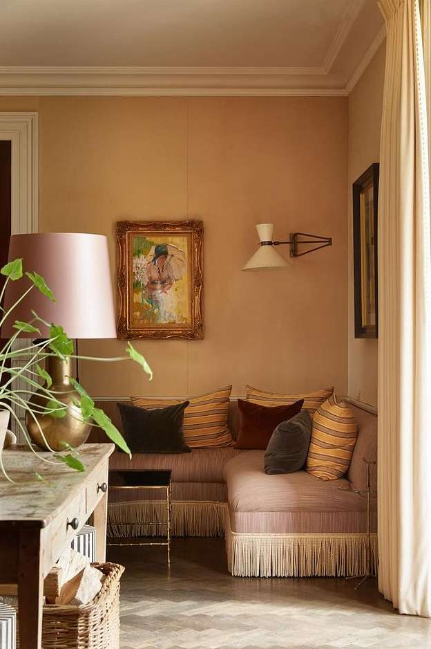 Interior corner featuring a fringe-trimmed L-shaped sofa with throw pillows, a lamp on a table, and a framed painting.