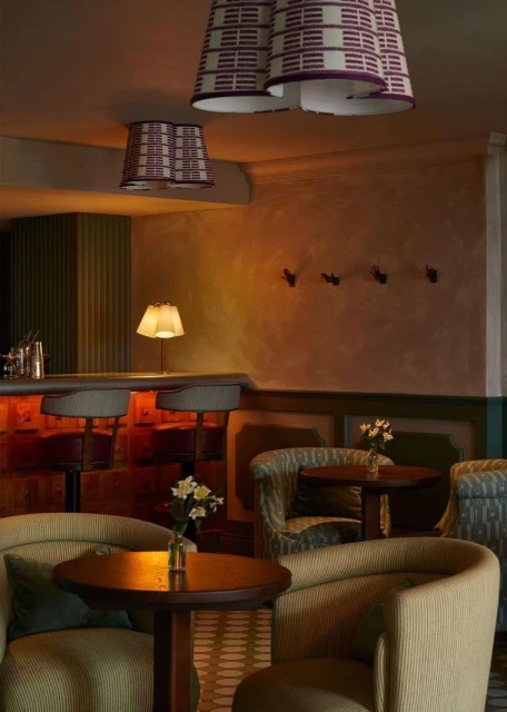 Interior design with bar, tables, and chairs in warm lighting. Patterned lampshades hang from the ceiling in cozy restaurant setting.