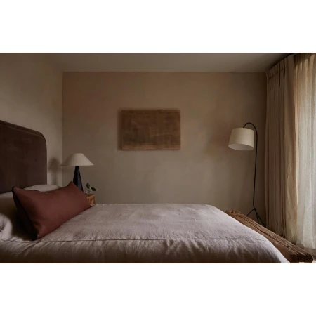 Minimalist bedroom with a queen bed, linen bedding, and a dark headboard. An abstract painting hangs above the bed in a neutral-toned room.