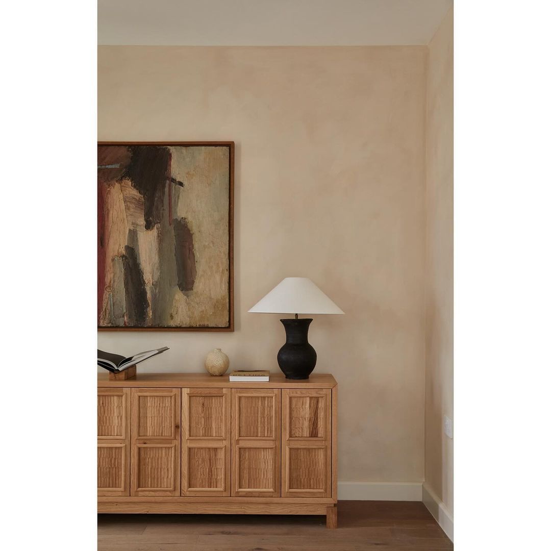 Interior design featuring a wooden cabinet with decor items including an abstract painting, table lamp, and books in a neutral palette.