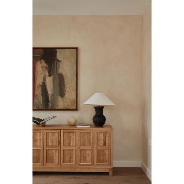 Interior design featuring a wooden cabinet with decor items including an abstract painting, table lamp, and books in a neutral palette.