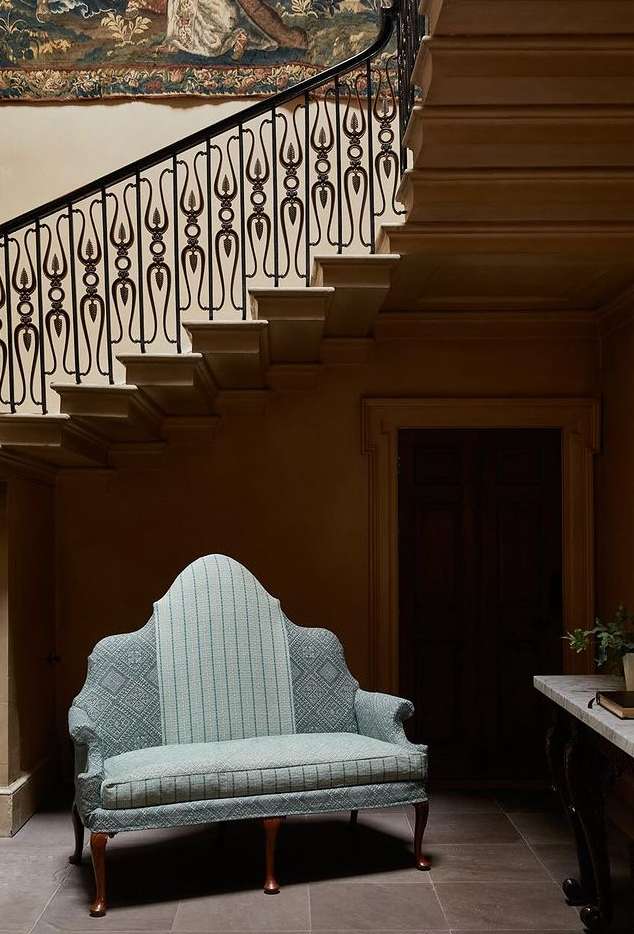 Elegant foyer featuring a staircase with ornate iron railing, a stylish settee with patterned upholstery, and a neutral color palette.