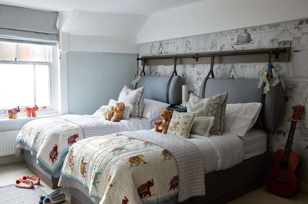 Bright children's bedroom featuring two beds with elephant-themed quilts, teddy bears, and a guitar, creating a cozy and playful space.