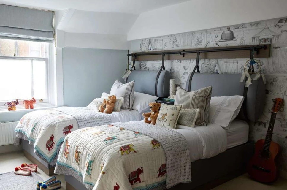 Bright children's bedroom featuring two beds with elephant-themed quilts, teddy bears, and a guitar, creating a cozy and playful space.