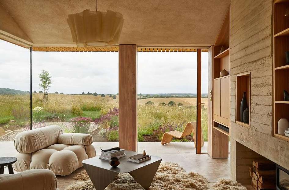 Contemporary living room interior with neutral tones, featuring a modular sofa, geometric table, and a view of a golden field.