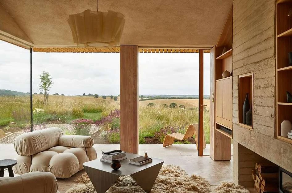 Contemporary living room interior with neutral tones, featuring a modular sofa, geometric table, and a view of a golden field.