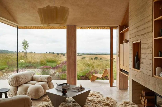 Contemporary living room interior with neutral tones, featuring a modular sofa, geometric table, and a view of a golden field.