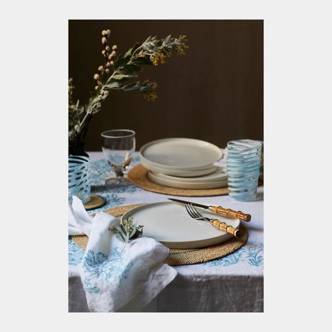 Table setting featuring plates, glassware, silverware, and floral arrangements on a tablecloth with a decorative pattern.