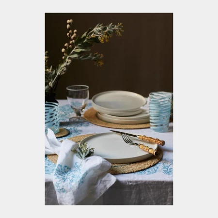Table setting featuring plates, glassware, silverware, and floral arrangements on a tablecloth with a decorative pattern.