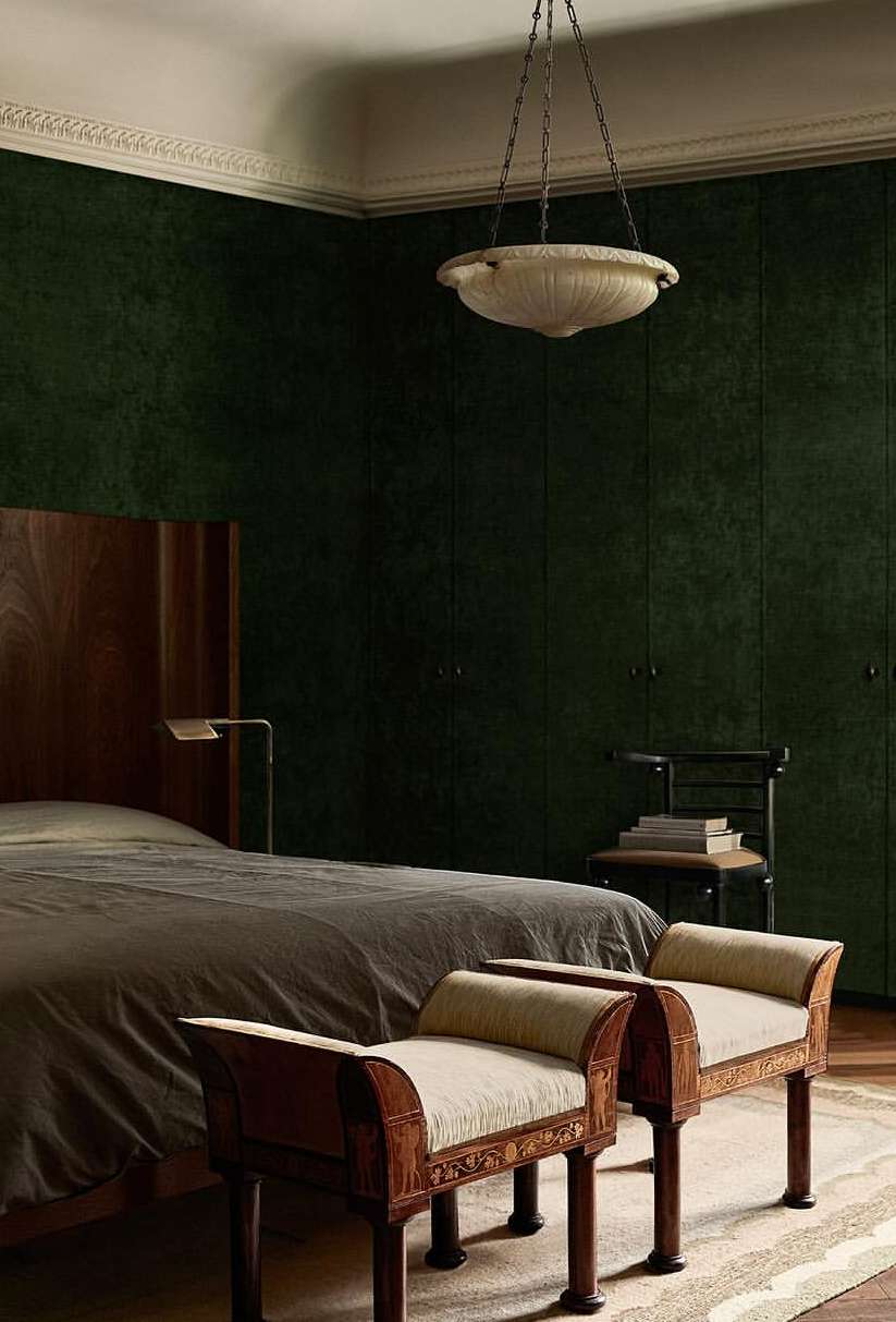 Bedroom interior features a bed, dark green paneled walls, two upholstered chairs, a stone lamp, and an overhead light fixture.