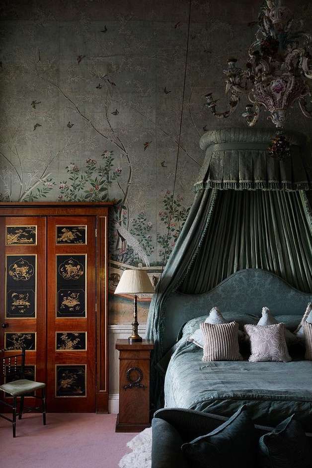 Elaborate canopy bed in an ornate bedroom featuring detailed wallpaper, decorative chandelier, and antique wooden closet with painted panels.