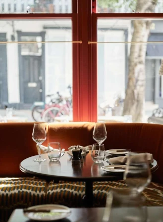 Elegantly set table in a restaurant with wine glasses and plates, featuring natural light through a window and a cozy booth.
