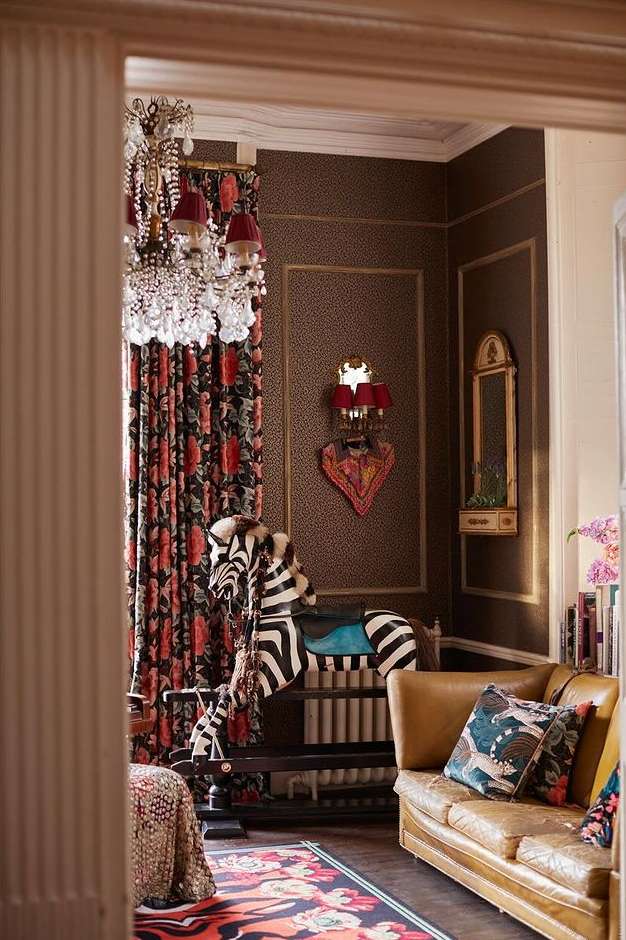 Interior view of a room featuring a zebra rocking horse, chandelier, couch, and patterned wallpaper in a cozy, eclectic style.