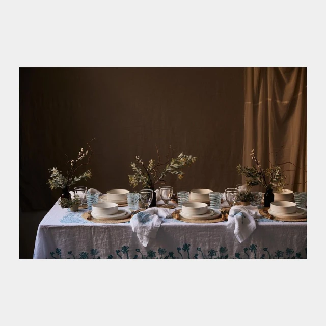 A beautifully set dining table features place settings with plates, glasses, and linens, decorated with floral arrangements, evoking a cozy, inviting ambiance.