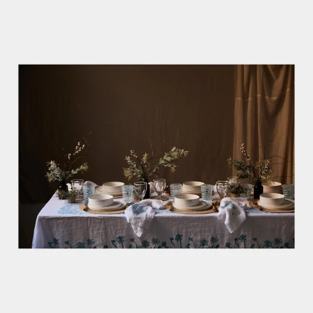 A beautifully set dining table features place settings with plates, glasses, and linens, decorated with floral arrangements, evoking a cozy, inviting ambiance.