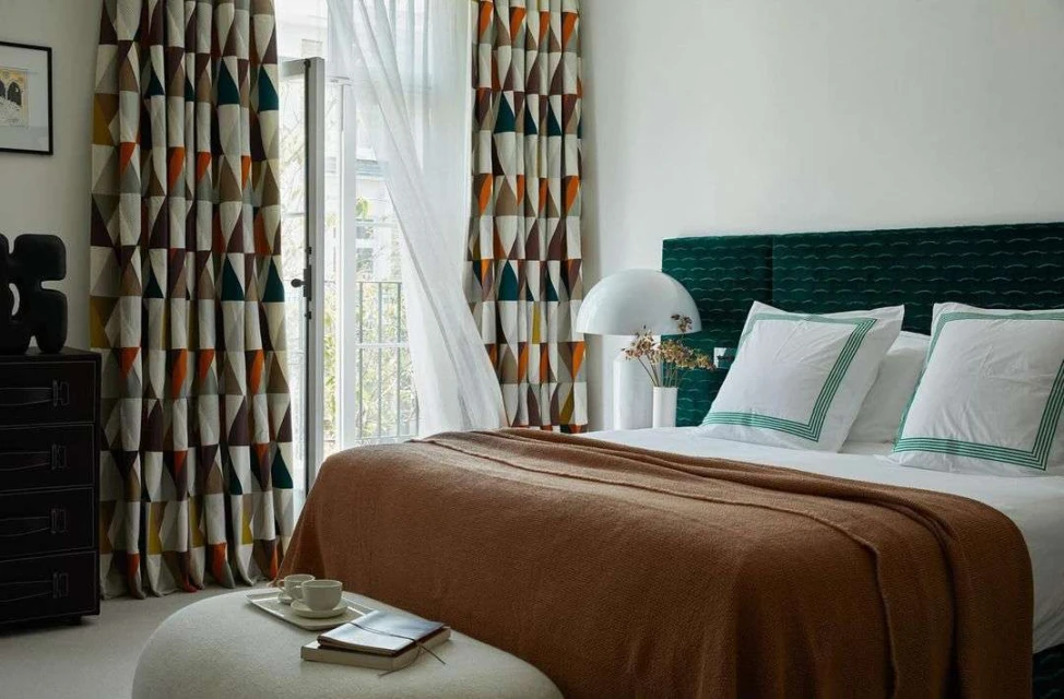 Bedroom interior showcasing bed with headboard, blanket, pillows, and decorative triangle-patterned curtains next to an open door.