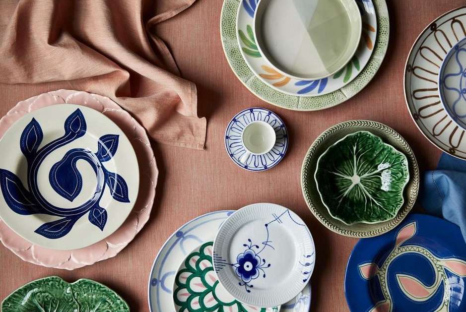 Overhead shot of an arrangement of decorative plates in various sizes and designs on a salmon-colored linen surface, creating an elegant table setting.