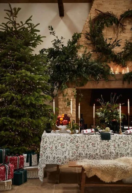 Festive dining room with Christmas tree, presents, and dining table set with candles and fruit, creating a warm, inviting atmosphere.