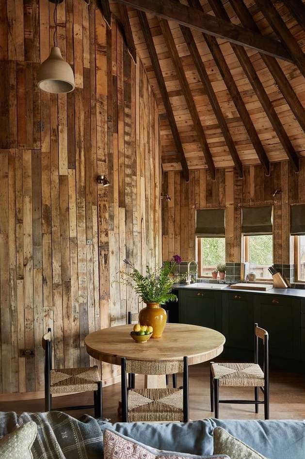 Indoor dining space featuring a wooden table with floral centerpiece, surrounded by chairs, set against a rustic wood-paneled wall and ceiling.