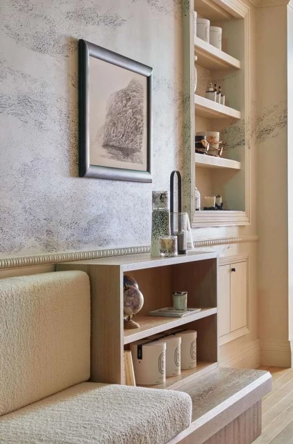 Modern interior with a beige built-in sofa, open shelving unit, and framed art hanging on a textured wall in a brightly lit room.