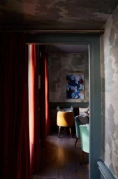 Interior view through a doorway into a warmly lit restaurant with velvet curtains, upholstered armchairs, and patterned walls.
