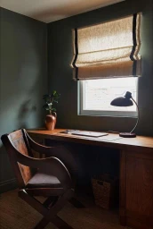 Interior shot of a home office with dark green walls, a wooden desk, and a dark wooden chair by Helen Cathcart