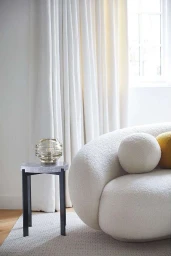 Curved cream bouclé sofa with a small glass lamp on a side table in a bright interior by Helen Cathcart
