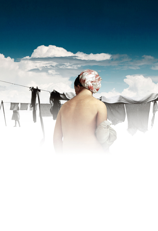 Adult woman wearing a headscarf stands near clothesline with hanging clothing against a blue sky with white clouds in an outdoor setting.