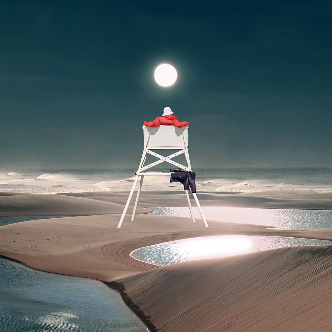 Person on a lifeguard tower on a beach at night under a bright light. White lifeguard tower with a red jacket and blue pants.