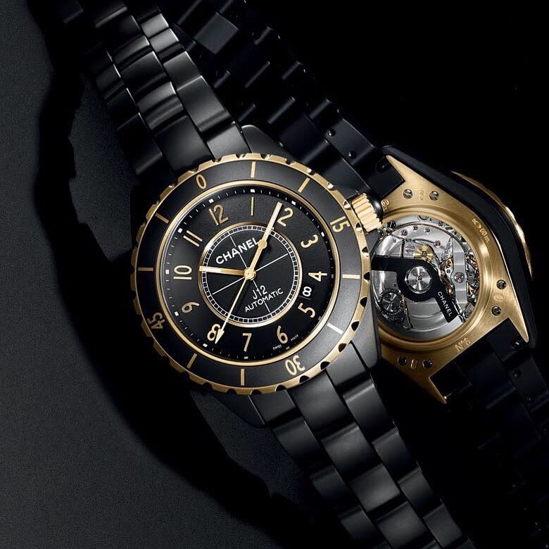A black ceramic Chanel J12 automatic watch with gold accents on a dark background, showcasing luxury timekeeping and modern elegance.