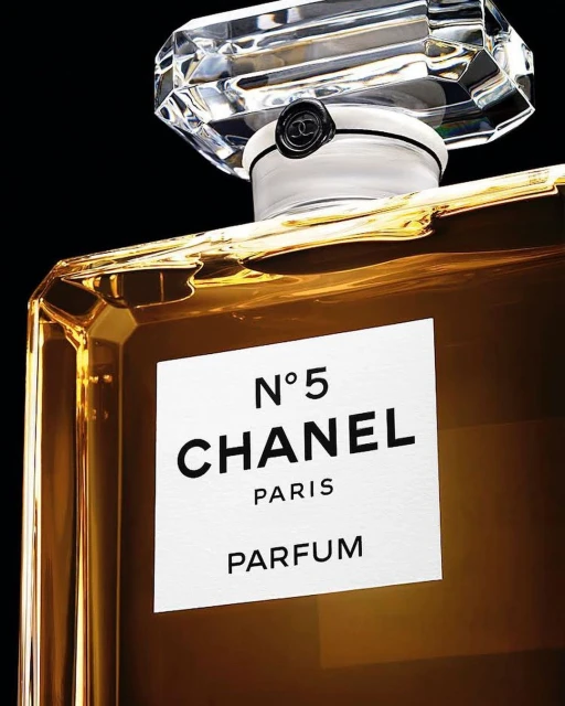 Close-up of a gold-colored Chanel No. 5 Parfum bottle against a black background, featuring a clear geometric cap and white label.