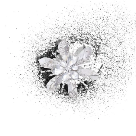 Close-up of a snowflake-shaped brooch made of silver and gems surrounded by black glitter on a white surface, creating a luxurious effect.