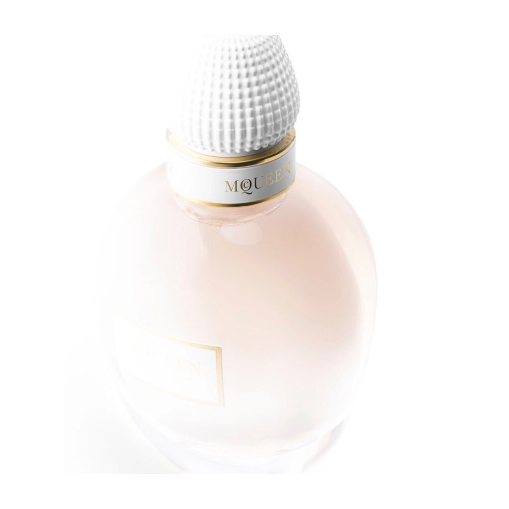 Round perfume bottle with white cap, featuring gold accents, displayed against a bright white background, conveying luxury and elegance.