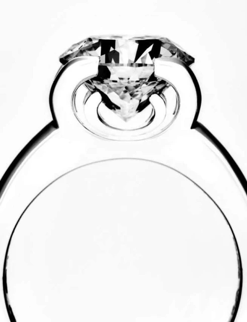 Close-up of a silver engagement ring featuring a clear diamond against a bright white background, showcasing its reflective facets.