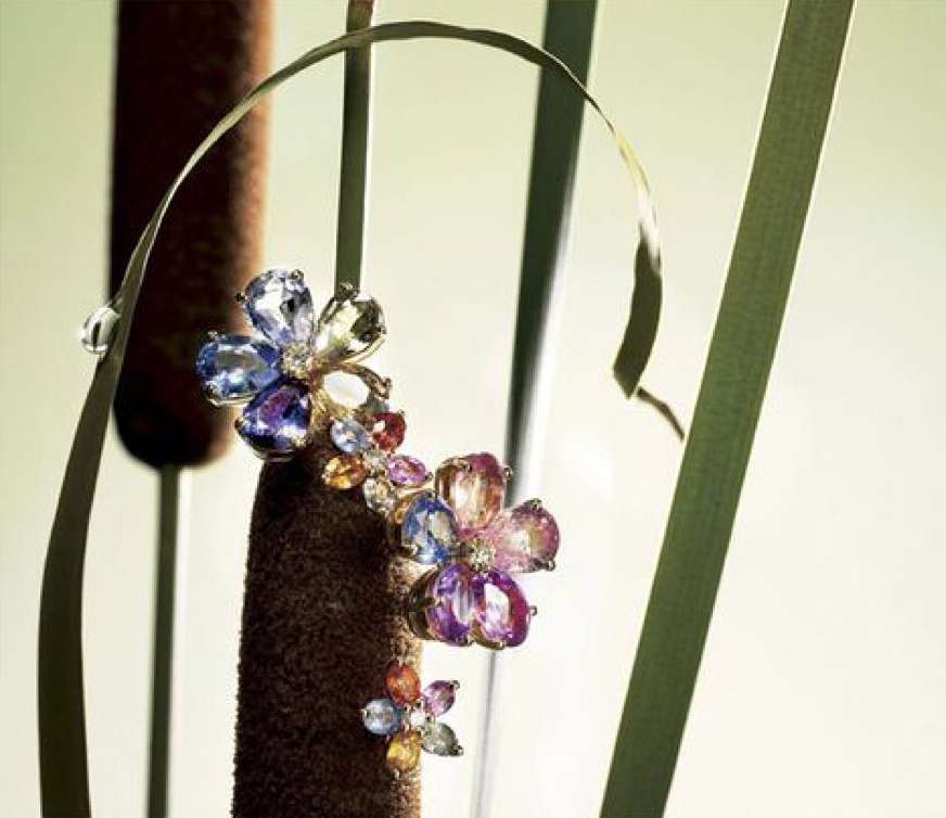 Close-up of flower-shaped jewelry adorning a brown cattail among green reeds, bathed in soft, diffused light, highlighting intricate gemstone detail.
