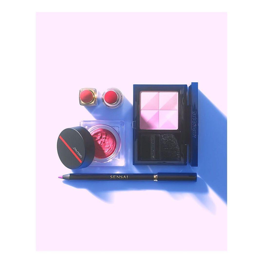 Flat lay studio shot of Shiseido and Givenchy beauty products including lipstick, blush, eye shadow, and eyeliner on pink backdrop.