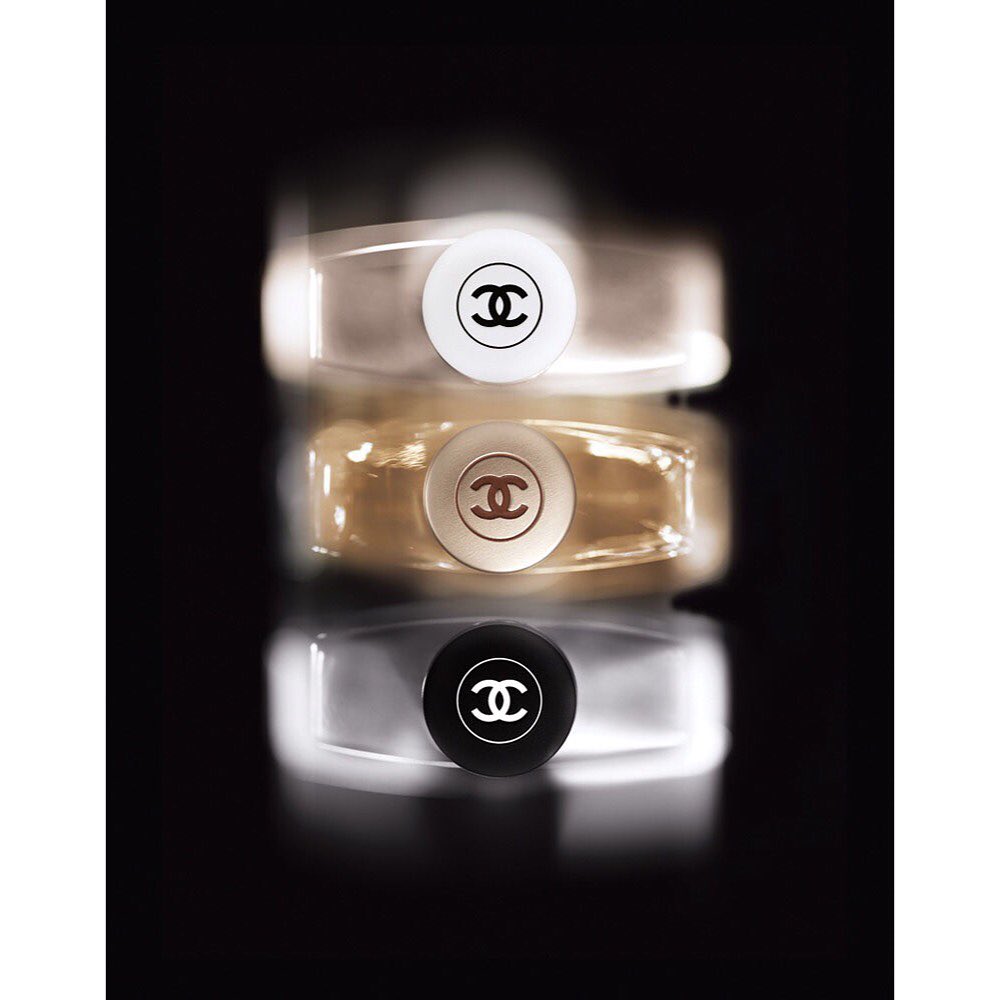 Close-up of stacked Chanel fragrance bottles with white, gold, and black tops against a dark background, showcasing luxury perfume design.