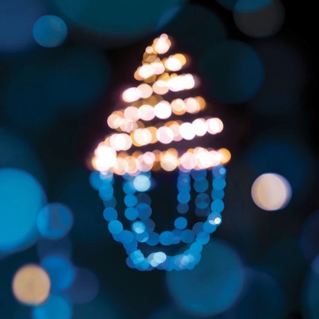 Defocused holiday lights arranged in a Christmas tree shape against a dark blue bokeh background, creating a festive abstract design.