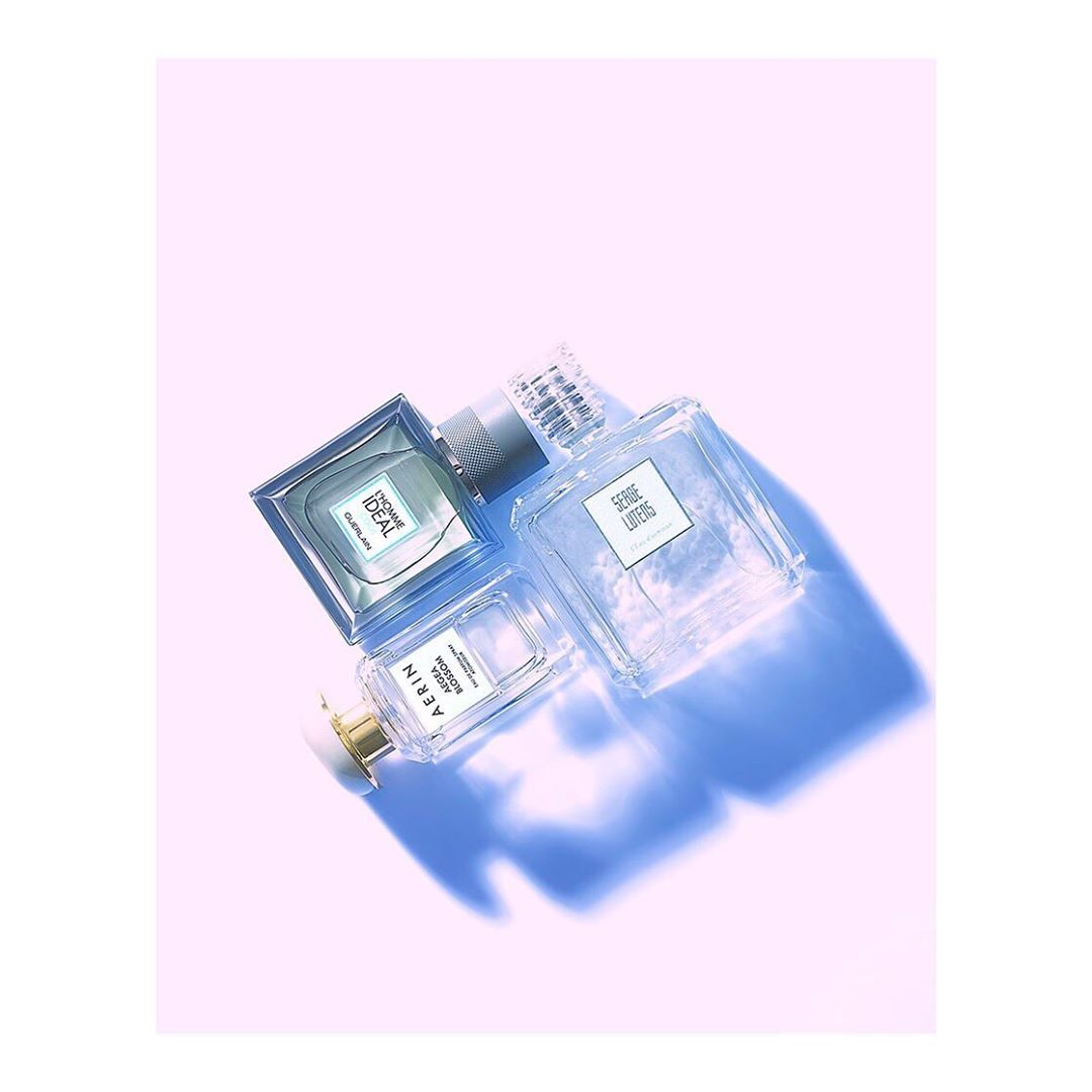 Three clear glass perfume bottles with different labels are arranged diagonally on a white surface with a light blue shadow.
