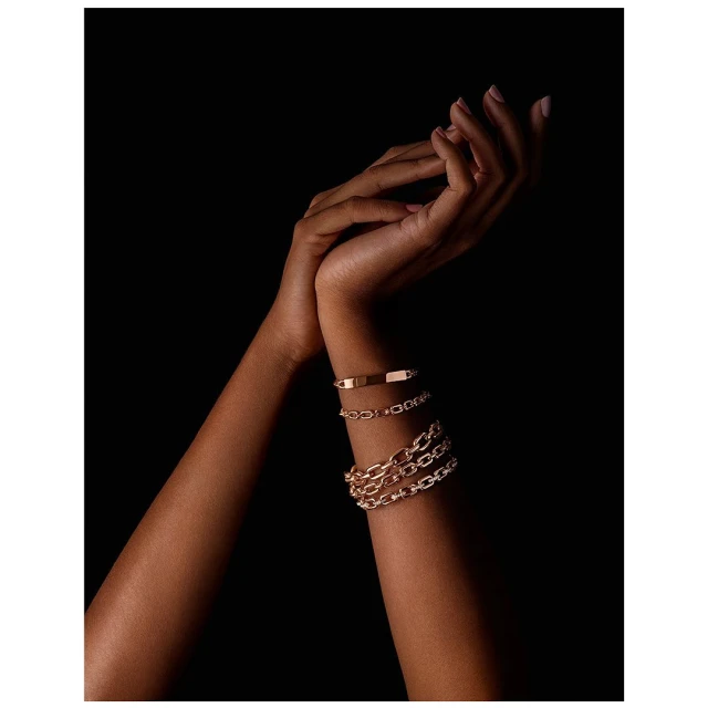 Close-up shot of a person's arms adorned with multiple golden bracelets against a solid black backdrop in a studio setting.