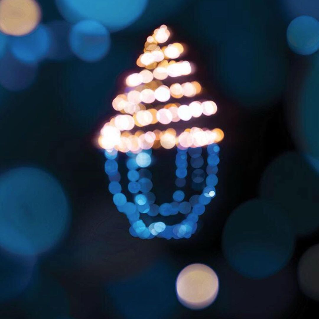 Abstract bokeh lights create a Christmas tree shape against a dark background, with glowing, out-of-focus orbs of light in blue and gold.