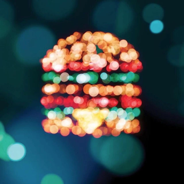 Blurred image of a burger-shaped light display with red, green, and yellow bokeh lights on a dark background, with a shallow depth of field.