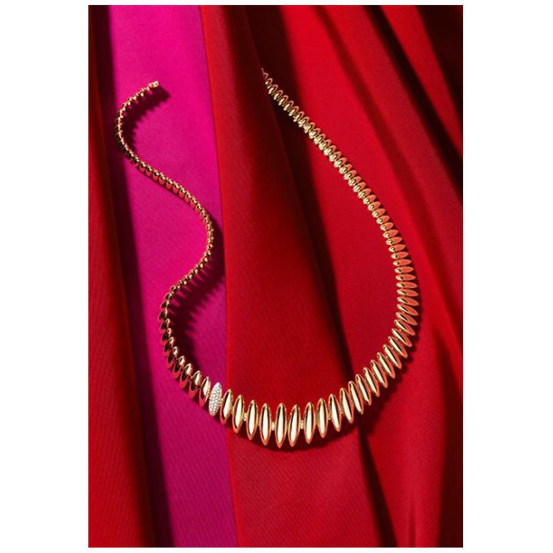 Elegant gold necklace with small diamonds on a red and pink draped fabric background. Close-up product shot for jewelry advertisement.